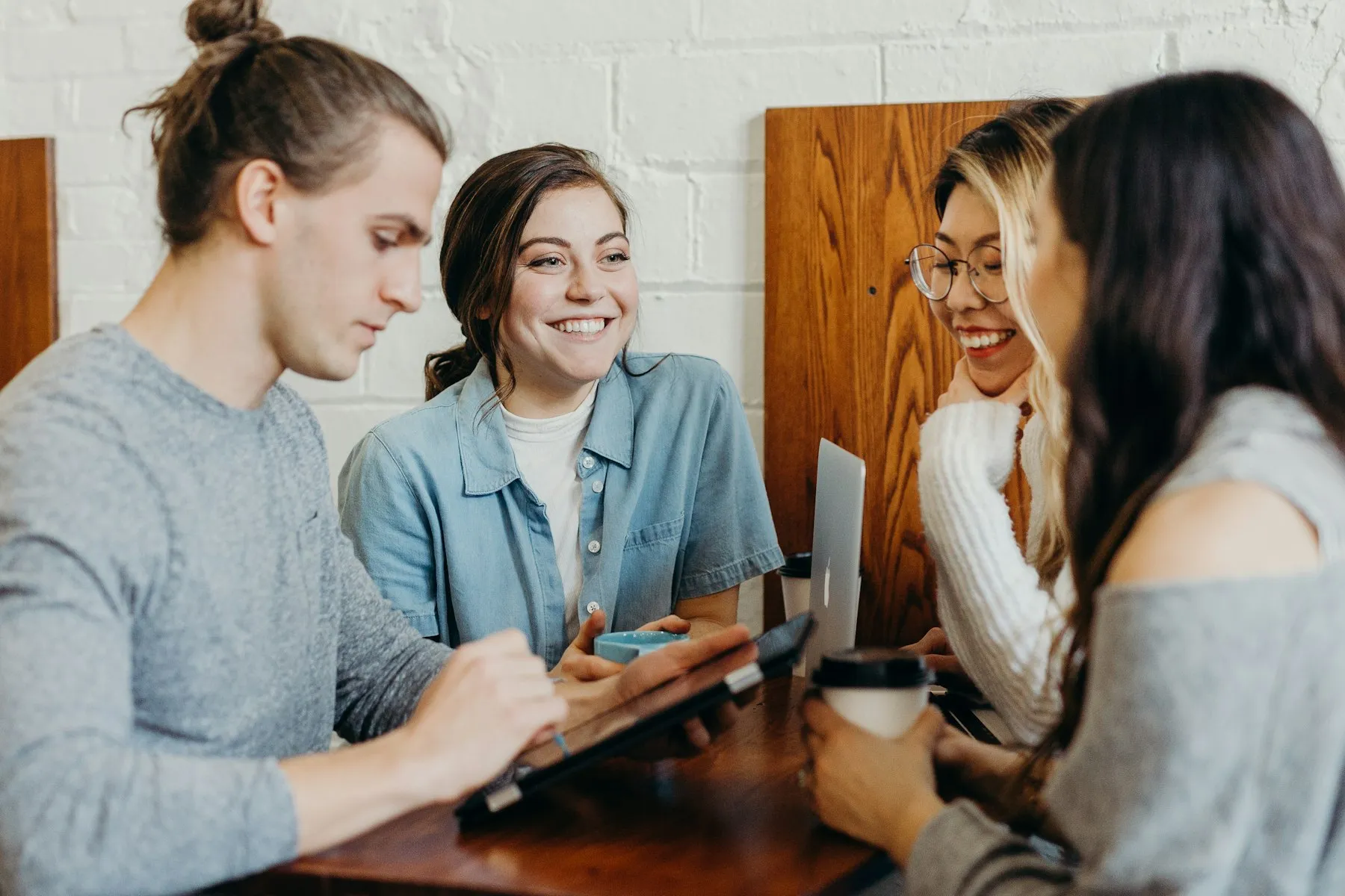 Four adults talking and laughing around a table with laptops and coffee