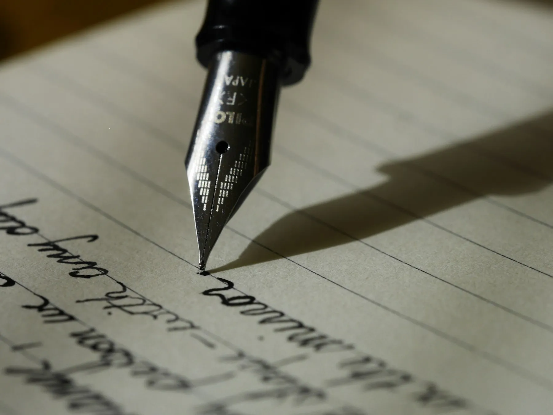 A fountain pen writing in cursive on lined paper