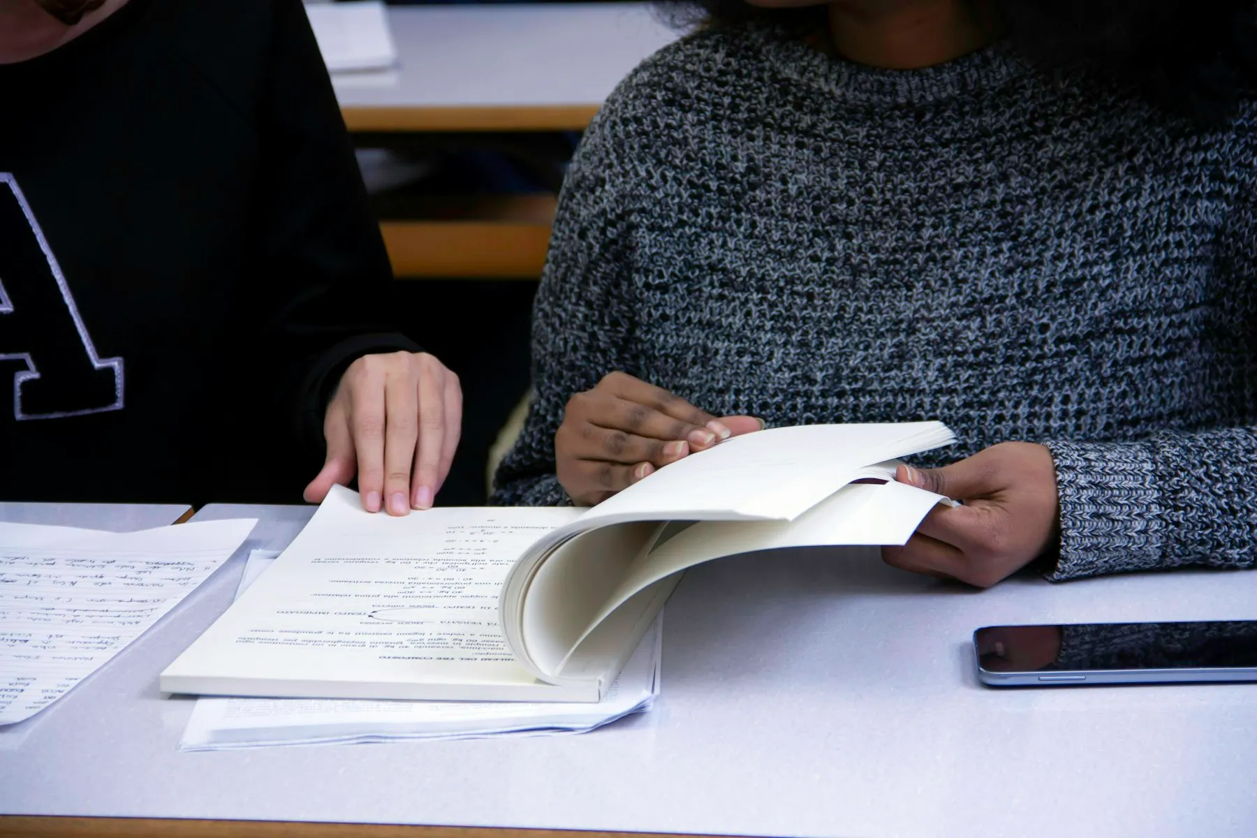 A tutor and a learner side by side, working through printed notes together